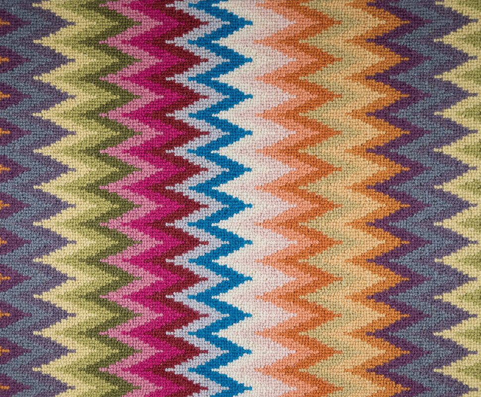 Close view of tight wool loop pile forming sharp zig-zag waves in electric blue, fuchsia, and yellow.